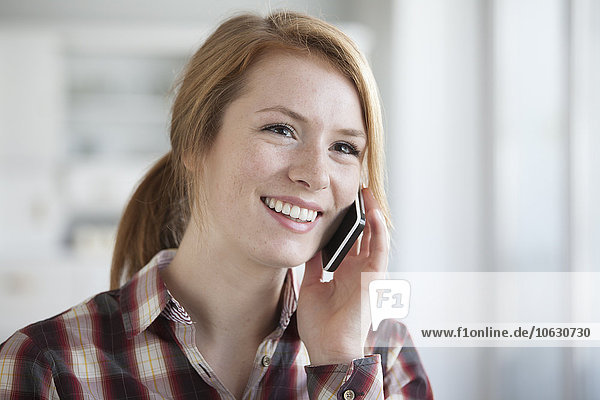 Porträt einer lächelnden jungen Frau beim Telefonieren mit dem Smartphone