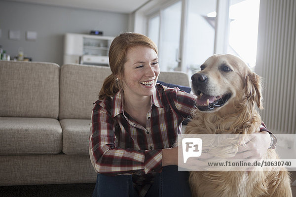 Porträt der lächelnden jungen Frau und ihres Hundes zu Hause
