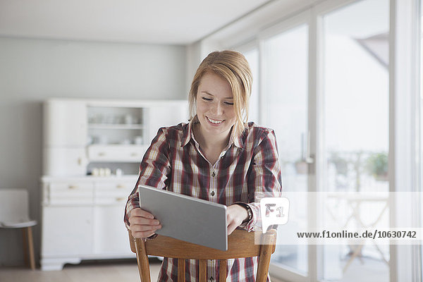 Porträt einer lächelnden jungen Frau mit ihrem digitalen Tablett zu Hause