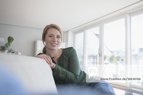 Porträt einer lächelnden jungen Frau  die zu Hause auf der Couch sitzt.