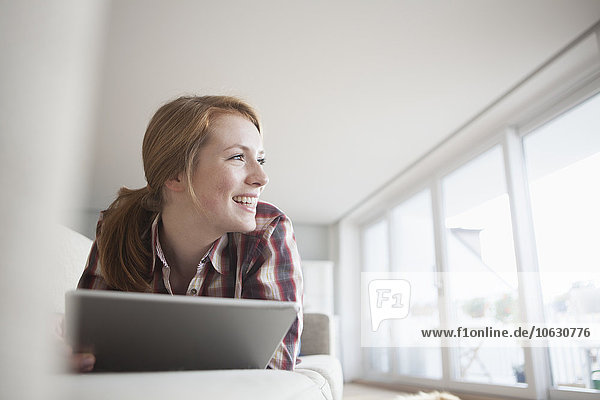 Lächelnde junge Frau auf der Couch liegend mit digitalem Tablett