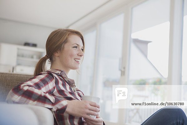 Smiling young woman relaxing with cup of coffee at home