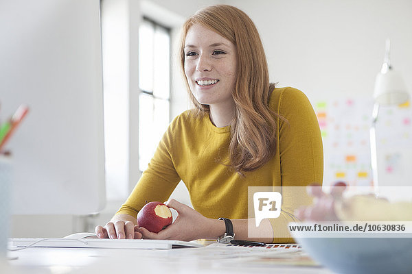 Junge Frau im Büro  die am Schreibtisch arbeitet und Apfel isst.