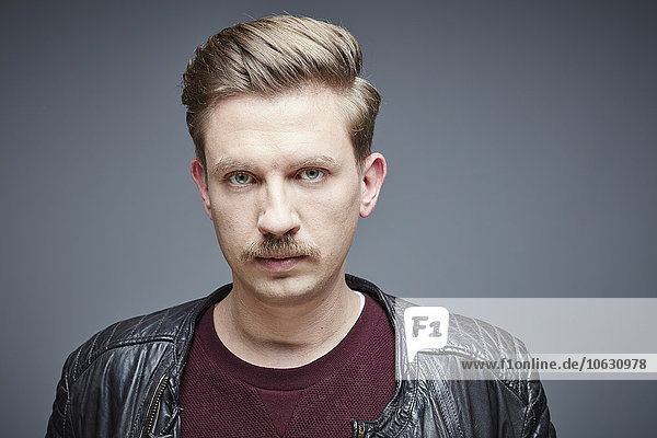Portrait of seriuos looking man with moustache in front of grey background