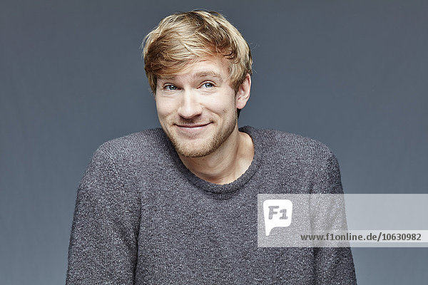 Portrait of smiling blond man in front of grey background