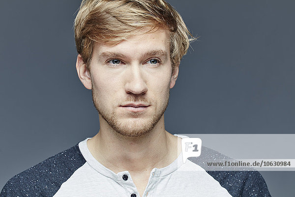 Portrait of young blond man in front of grey background