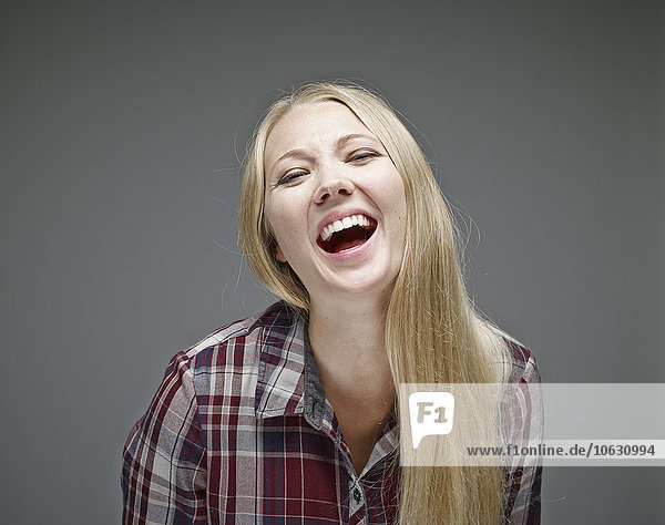 Porträt der lachenden jungen Frau vor grauem Hintergrund