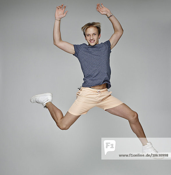 Porträt eines jungen Mannes,  der vor grauem Hintergrund in die Luft springt.