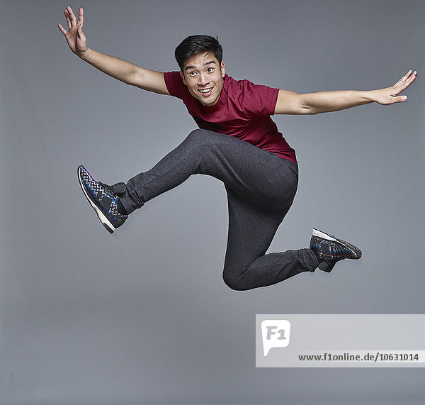 Porträt eines jungen Mannes  der vor grauem Hintergrund in die Luft springt.