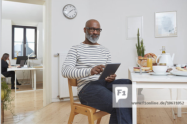 Portrait of smiling man sitting at breakfast table with digital tablet