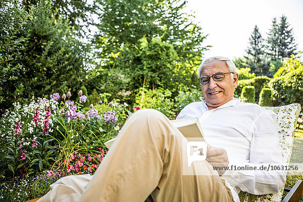 Lächelnder älterer Mann liest Buch im Garten