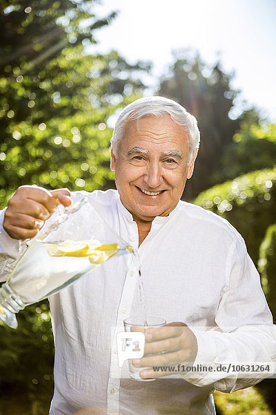 Lächelnder älterer Mann gießt Wasser ins Glas im Garten