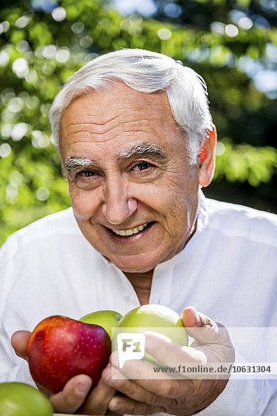 Smiling senior man holding apples outdoors