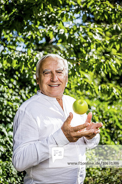 Lächelnder älterer Mann mit Apfel im Garten