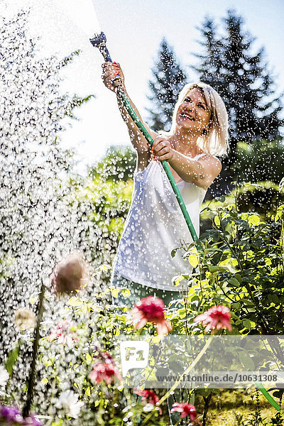 Smiling mature woman watering flowers in garden