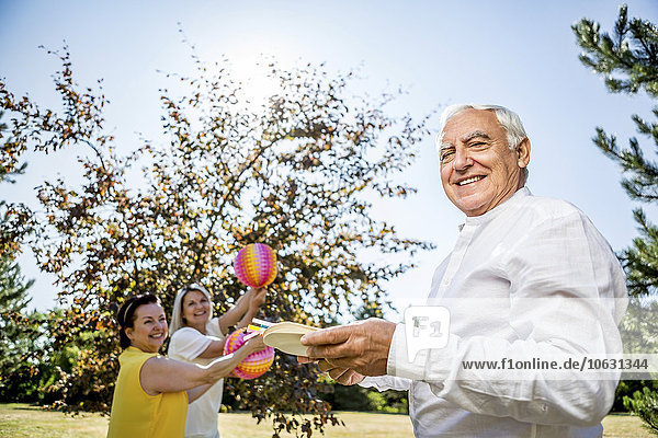 Portrait of smiling senior man with paper plates on meadow with women in background