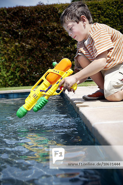 Little boy kneeling with his water gun at pool edge