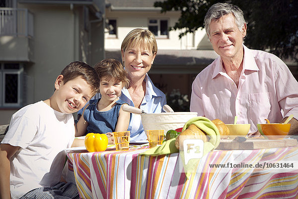 Familienporträt des kleinen Jungen und Mädchens mit den Großeltern am Esstisch im Garten