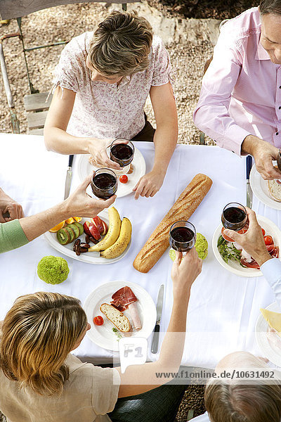 Spanien  Mallorca  fünf Freunde sitzen am gedeckten Tisch im Garten und rösten mit Rotwein.