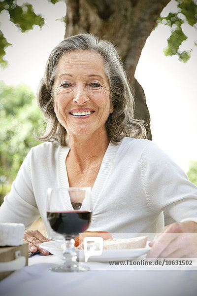 Porträt einer lächelnden Frau  die am gedeckten Tisch im Garten sitzt.