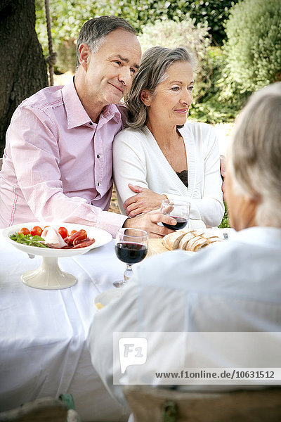 Porträt eines reifen Paares  das Seite an Seite am gedeckten Tisch im Garten sitzt.