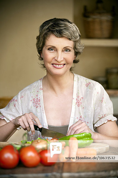 Porträt einer lächelnden Frau beim Gemüsehacken