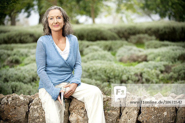Spanien  Mallorca  Portrait einer reifen Frau  die auf einer Wand im Garten sitzt.