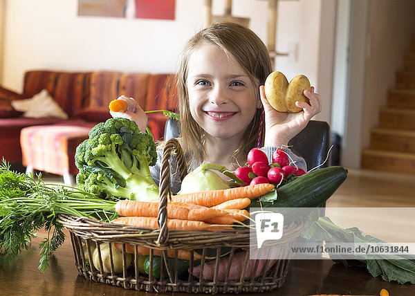 Porträt des grinsenden Mädchens mit Korb mit frischem Gemüse zu Hause