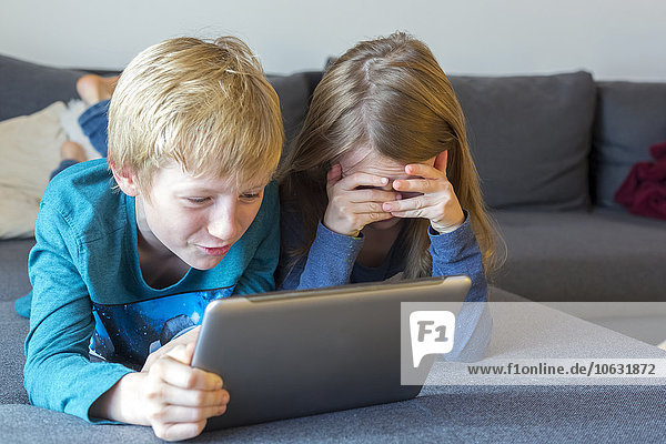 Junge und Mädchen auf der Couch liegend mit digitalem Tablett