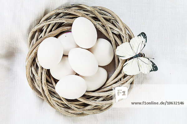 Weiße Eier im Weidennest und Schmetterlingsdekoration