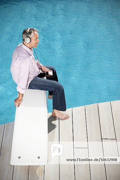 Spain  Mallorca  man sitting on springboard of a pool listening music with headphones