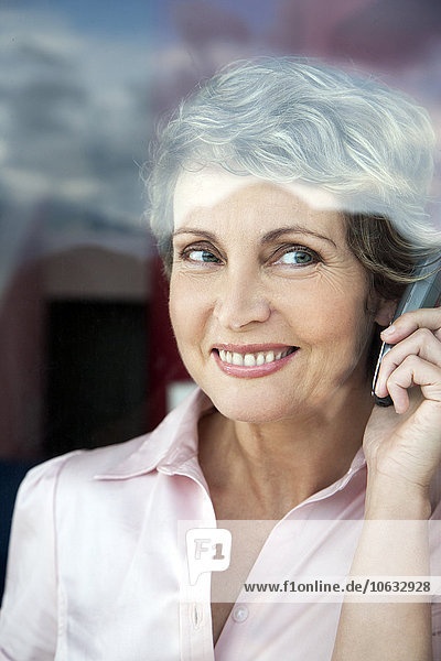 Portrait of smiling woman telephoning while looking through the window