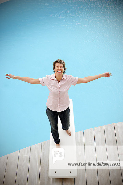 Portrait of happy woman standing on springboard with arms outstretched