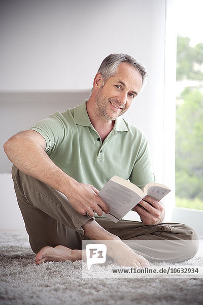 Portrait of smiling man with book sitting on a carpet at home