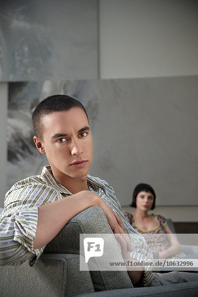 Young man sitting on couch with woman in background