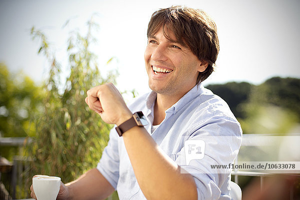 Lachender Mann mit Tasse Kaffee auf dem Balkon in einer Smartwatch