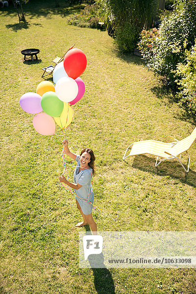 Happy woman standing in garden holding colorful balloons