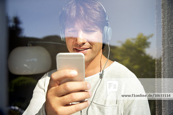 Man behind windowpane listening to music from smartphone