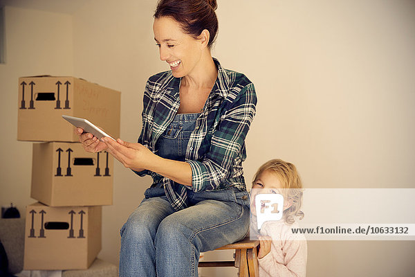 Laughing woman with daughter looking at digital tablet with cardboard boxes in background