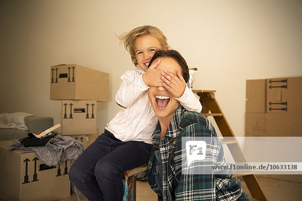 Daughter covering mother's eyes with cardboard boxes in background