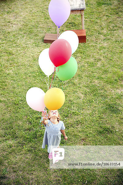 Mädchen steht im Garten und hält bunte Luftballons.