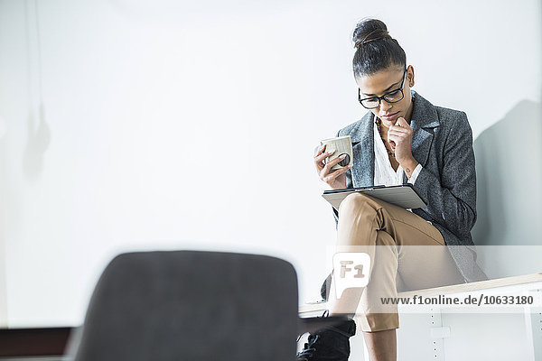 Junge Frau im Büro mit Tasse Kaffee und digitalem Tablett