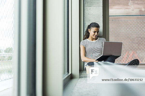Junge Frau sitzt auf dem Boden im Büro mit Laptop