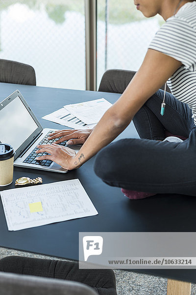 Junge Frau sitzt auf dem Konferenztisch mit Laptop