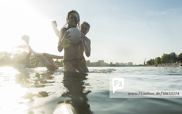 Zwei glückliche Paare mit Ball im Wasser