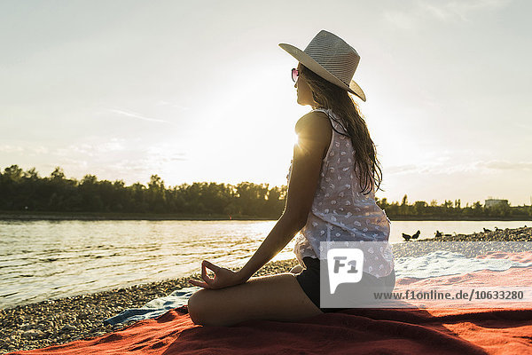 Junge Frau beim Yoga am Flussufer bei Sonnenuntergang