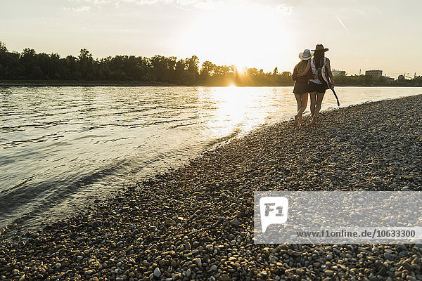 Two friends walking at the riverside at sunset
