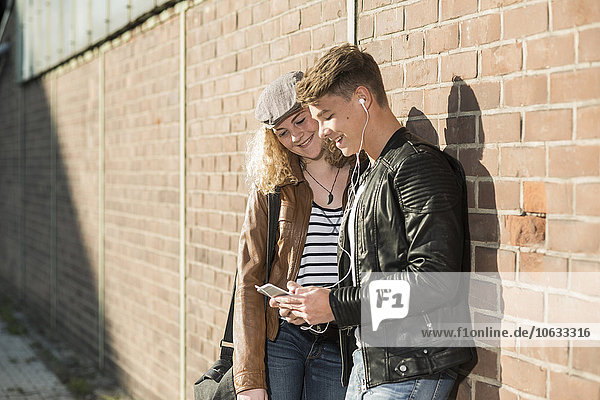 Relaxed young couple with cell phone and earbuds outdoors