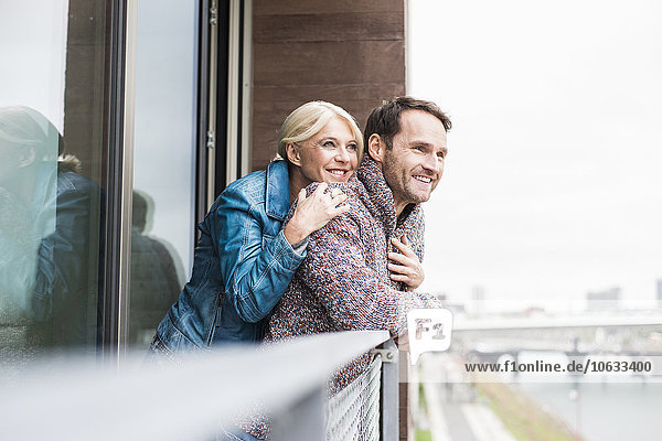 Ein glückliches Paar steht zusammen auf dem Balkon und schaut in die Ferne.