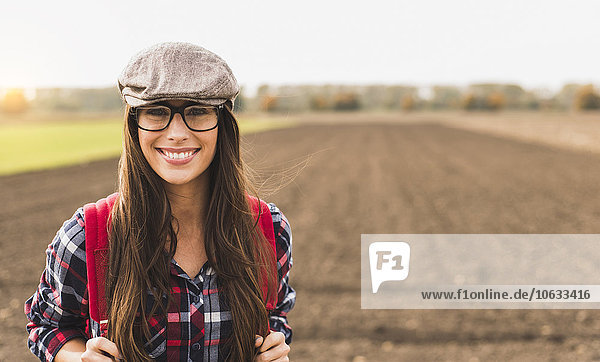 Porträt einer lächelnden jungen Frau mit Rucksack auf dem Land